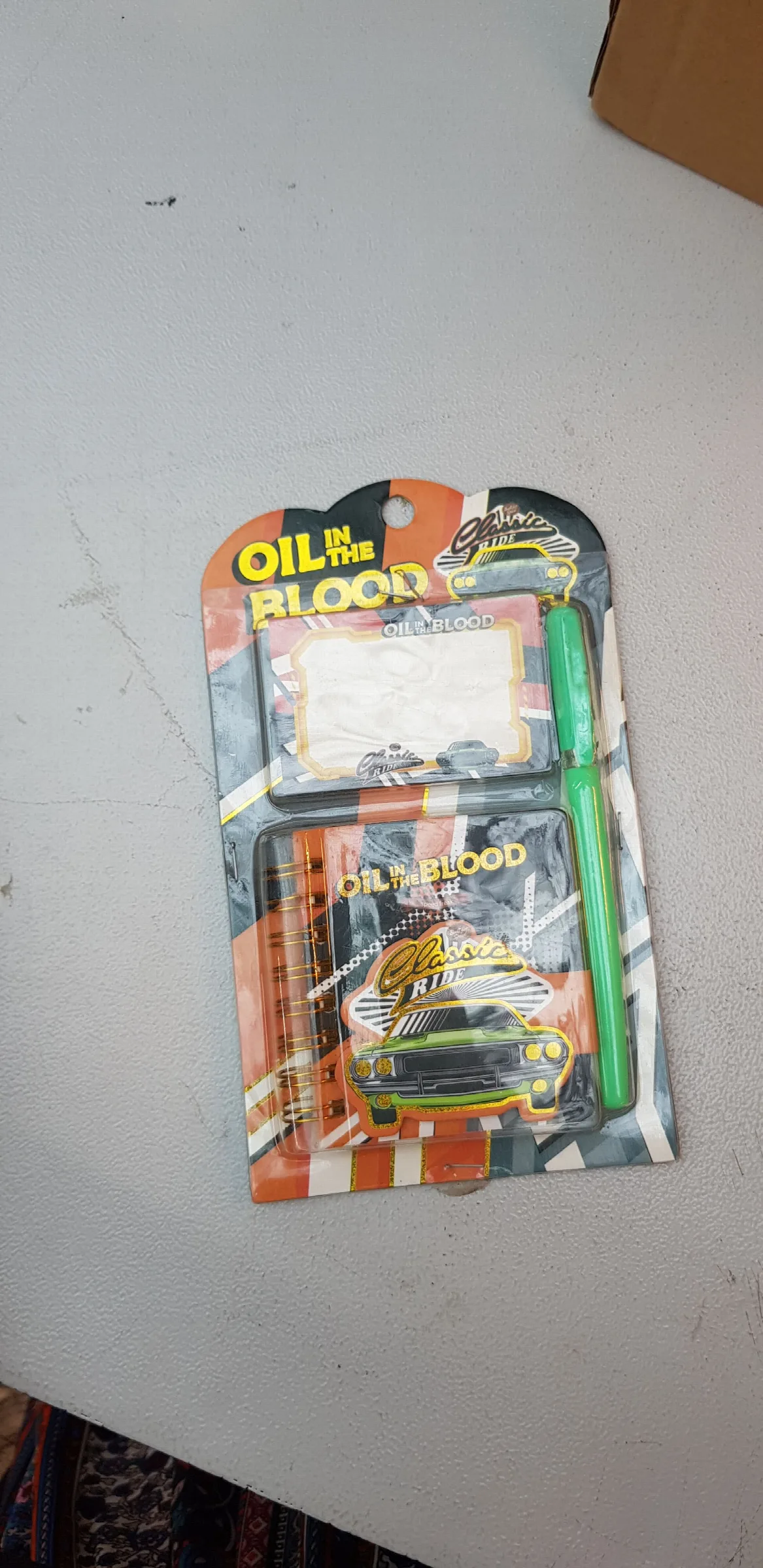 shows a stationary set featuring an "Oil in the Blood" muscle car design, which includes a pocket-sized spiral notebook, a small notepad, and a green pen